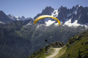 A paraglider gracefully flies over rocky mountain peaks on a sunny day, offering a sense of adventure and freedom.